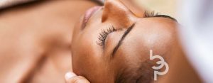 Black girl with closed eyes relaxing in outdoor spa while preparing for microneedling treatment.